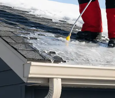 Ice dam removal technician using a steam wand to melt thick ice buildup on a residential roof in Jackson, MS