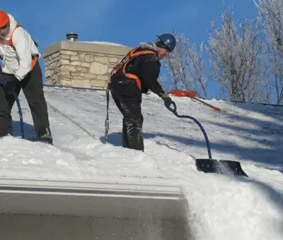 Professional technicians performing roof snow removal with safety harnesses and shovels in Jackson, MS